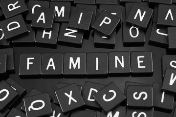 Black letter tiles spelling the word "famine" on a reflective background