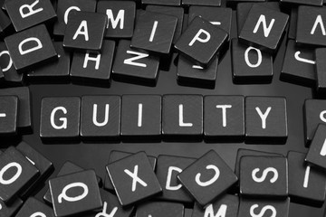 Black letter tiles spelling the word "guilty" on a reflective background