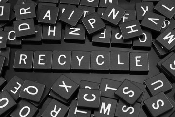 Black letter tiles spelling the word "recycle" on a reflective background
