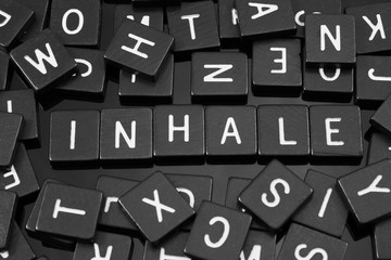 Black letter tiles spelling the word "inhale" on a reflective background