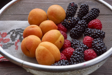 colander with the washed-up berries raspberry and blackberry and apricots