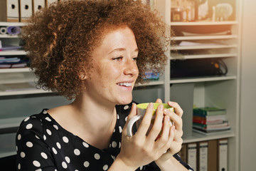 jeune femme rousse stagiaire travaillant dans un bureau en souriant et buvant un café