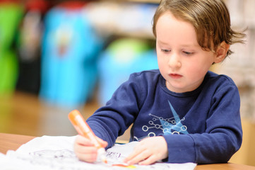 Young boy sitting down at desk indoors coloring with markers