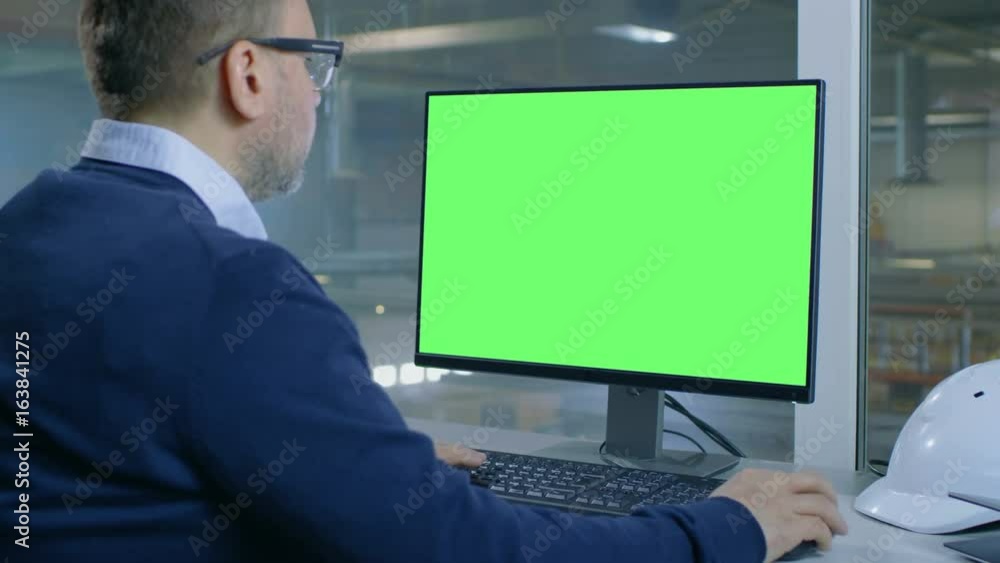 Poster chief engineer works on his computer with mock-up green screen. inside of the factory is seen from h