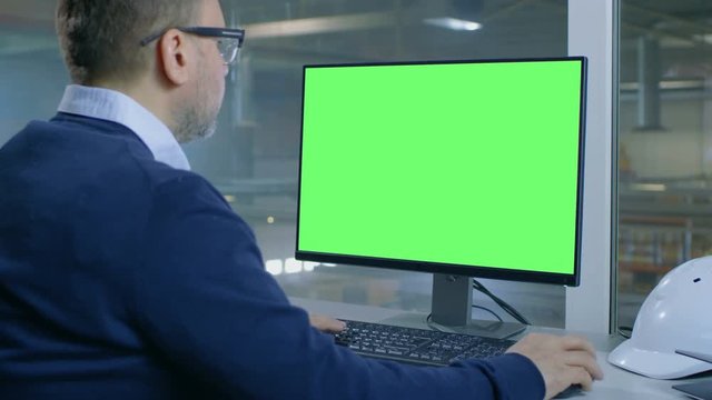 Chief Engineer Works on His Computer with Mock-up Green Screen. Inside of the Factory is Seen From Her Office Window.Shot on RED EPIC-W 8K Helium Cinema Camera.