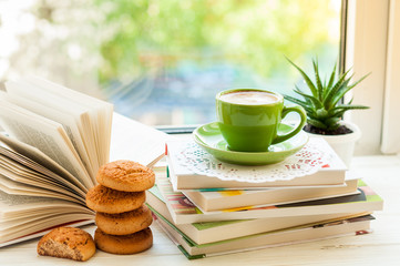 Coffee cup, open book, cookies and flower on window with bokeh. Reading and breakfast. Concept cozy home