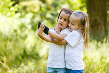 Two small laughing girls do selfie on a smartphone