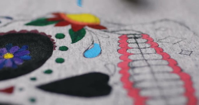 close-up macro shooting drawing colorful mexican mask. young woman's hand draws on material. girl is drawing on clothes. oilpaintig creative time in the art studio. blue paint color