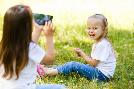 Little girl makes photos of her sister with smartphone outdoors.