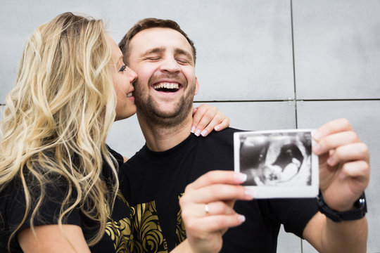 A married couple is happy with pregnancy, an ultrasound picture of a baby in the hand. Artificial insemination.