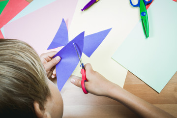 Boy cutting colored paper with scissors at the table