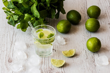 Mojito cocktail with lime, mint and ice on white wooden background.