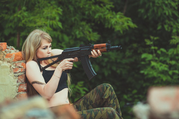 Portrait of a beautiful girl in camouflage in her arms during a war is aiming at a target or an enemy because of shelter