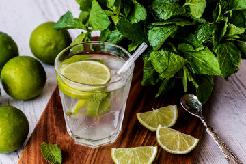 Mojito cocktail with lime, mint and ice on white wooden background.