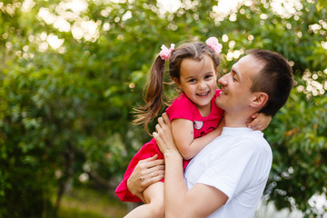 Happy joyful young father with his little daughter. Father and little kid having fun outdoors in orchard garden, playing together in summer park. Dad with his child laughing and enjoying nature