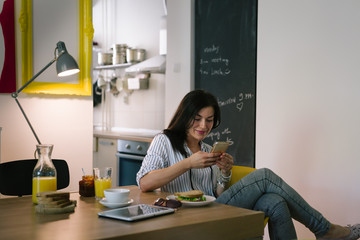 Relaxed morning. woman having breakfast and texting message on her phone