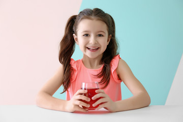Cute little girl with glass of juice sitting at table, on color background © Africa Studio