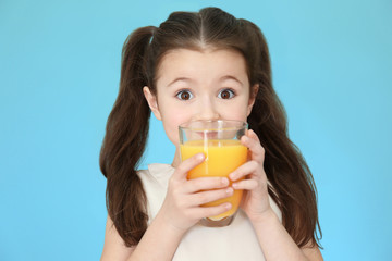 Cute little girl drinking juice on color background