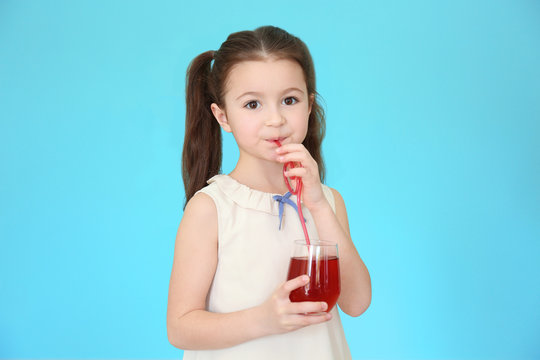 Cute little girl drinking juice on color background