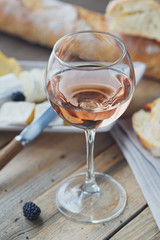 A glass of rose wine served with cheese plate, blackberries and baguette