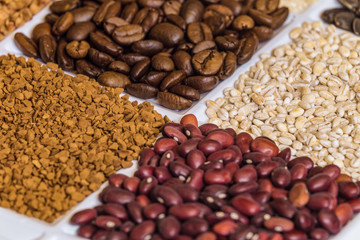 Fototapeta premium Set of groceries laying horizontal perspective with limited depth of field: roasted coffee beans, pearl barley, freeze-dried instant coffee, dried red seeds of beans.