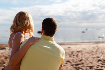 Young beautiful couple hugging with her back to the shore amid rocks and sea, enjoy the sunset and freedom. Journey to the sea.