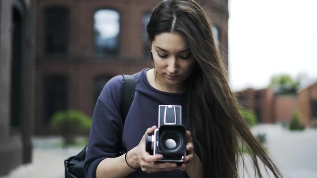 Front view of a young and pretty black haired woman holding an old fashioned camera and taking pictures. Locked down real time close up shot