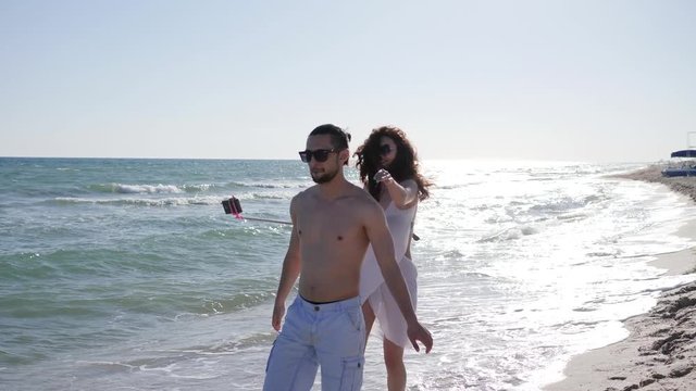 selfi photo couple on vacation, Friends have fun in travel, cheerful girl jumping on guy's back, Mobile phone on selfie stick removes funny photos of young people at ocean coast, love on beach