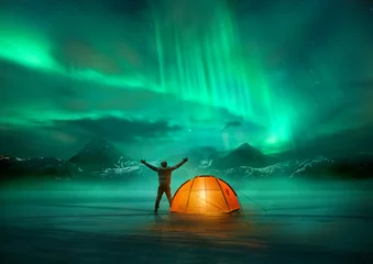 Fotobehang Noorderlicht Een man die kampeert in de wilde noordelijke bergen met een verlichte tent die een spectaculair groen noorderlicht-aurora-display bekijkt. Foto compositie.