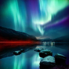 A large Northern Lights (aurora borealis) display glowing over a mountain pass and reflected on a...