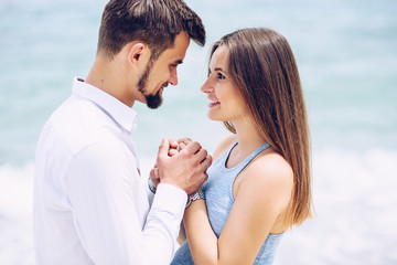 A beautiful pregnant woman in a blue dress and her courageous and handsome husband in a shirt and blue trousers leaned to each other against the background of the sea.