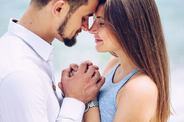 Naklejka premium A beautiful pregnant woman in a blue dress and her courageous and handsome husband in a shirt and blue trousers leaned to each other against the background of the sea.