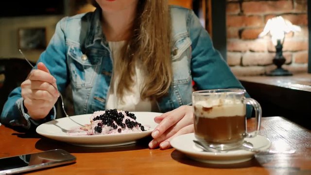 Pretty girl in a cotton jacket eats dessert with a hot chocolate in a cafe. Vintage interior. Brick wall.