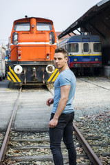 Handsome young man in blue t-shirt in front of train, looking at camera, turning around