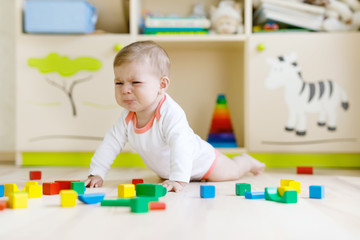 Cute sad crying baby playing with colorful wooden blocks toys