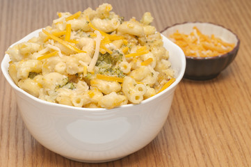 Macaroni and cheese casserole with a small side bowl of cheddar cheese to add, out of focus to leave attention on the large bowl