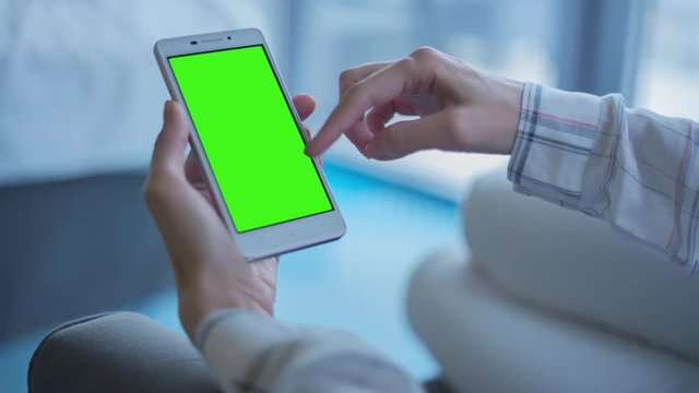 Young Woman in white jeans laying on couch uses smartphone with pre-keyed green screen. Few types of gestures - scrolling up and down, tapping, zoom in and out. Perfect for screen compositing