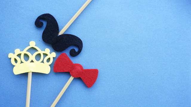 Top or flat lay view of Photo booth props a black mustache, a yellow crown and a red bow tie on a blue background flat lay. Birthday parties and weddings.