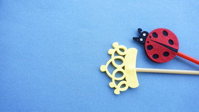 Top or flat lay view of Photo booth props a ladybird and a yellow crown on a blue background flat lay. Birthday parties and weddings. - Powered by Adobe