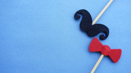 Top or flat lay view of Photo booth props a black mustache and a red bow tie on a blue background flat lay. Birthday parties and weddings.