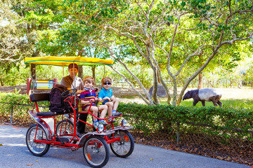 Fototapeta premium dad and two little kid boys biking on bicycle in zoo with animal