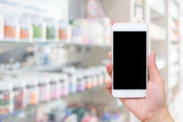 Woman hand hold blank screen mobile smartphone over medicine on Pharmacy store shelves