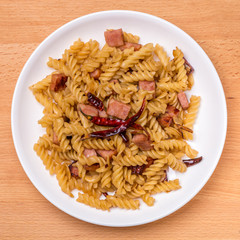 Asian tasty dish, stir-fried fusilli pasta with sliced bacon, garlic and dried chili hot & spicy style on wooden board background.