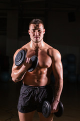 Fototapeta na wymiar Athletic shirtless young male fitness model holds the dumbbells.