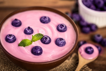 close up the  pink creamy homemade blueberries fruit yogurt with fresh green mint leaf on wooden table background