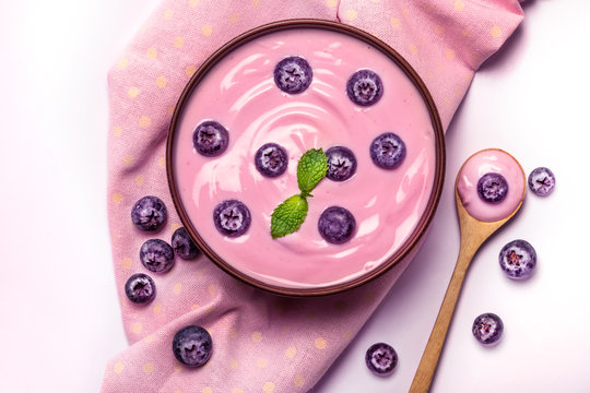 Close Up Pink Creamy Homemade Blueberries Fruit Yogurt With The Fresh Green Mint Leaf On White Background , Top View Or Overhead Shot