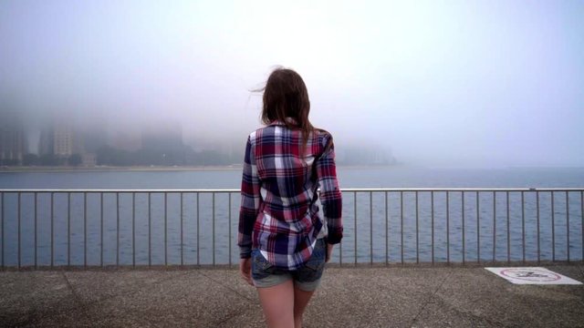 Walking Woman Looking On Ocean City Fog. Back View Of Woman Coming To Embankment. Young Woman Walking Out Of Ocean In Foggy Weather. Woman Going To Sea City. Loneliness In City