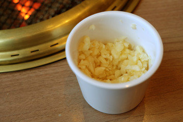 Minced garlic in a white cup beside a grille on fire chacoal