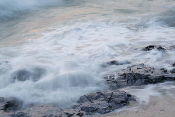 Soft waves hitting the rocks by the ocean, silky waves hitting the beach from long exposure.