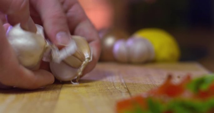 Man breaks apart head of garlic on wooden chopping kitchen board